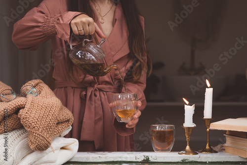 Warm and cosy hygge concept with white and beige sweaters, woman pouring tea, burning candles