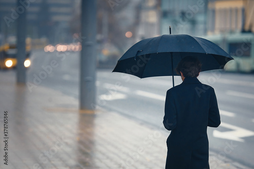 Stylish man with umbrella in rainy foggy day walking alone down the city street. Person with umbrella stands by road in rainy weather. Young man with black umbrella, rainy weather © Tricky Shark