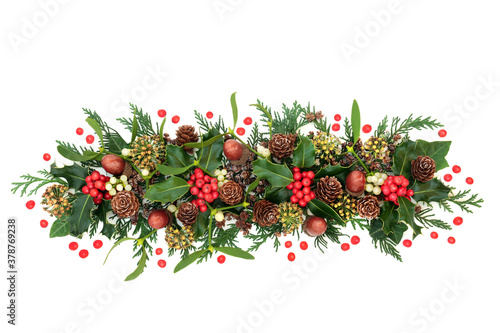 Natural winter floral decoration with holly, loose red berries, ivy, mistletoe, cedar cypress leaves, pine cones & acorns on white background. Traditional nature theme for Christmas & New Year.