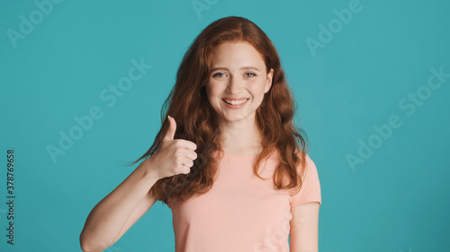 Pretty cheerful girl happily showing thumb up gesture on camera over colorful background. Well done expression
