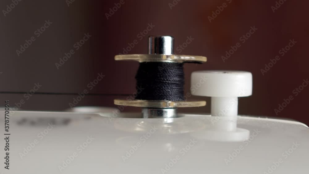 Close-up of automatic thread winding on a sewing machine bobbin. Winding a black thread on a small spool. Seamstress uses auto winding thread on the bobbin of a sewing machine Close-up of automatic thread winding on a sewing machine bobbin. Winding a black thread on a small spool. Seamstress uses auto winding thread on the bobbin of a sewing machine