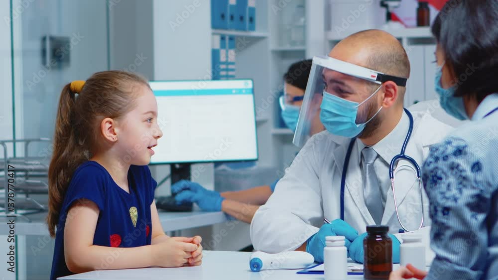 Doctor talking with child wearing protection mask during coronavirus. Pediatrician specialist in medicine providing health care services, consultation, treatment, examination in hospital cabinet. Doctor talking with child wearing protection mask during coronavirus. Pediatrician specialist in medicine providing health care services, consultation, treatment, examination in hospital cabinet.