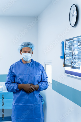 Doctor in scrubs looking to camera. Latex gloves on hands and mask on face. MRI enlighted board on the background. photo