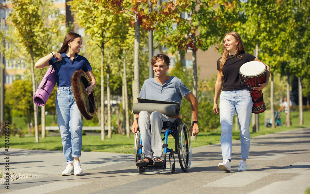 Obraz premium Summer. Happy caucasian handicapped man on a wheelchair spending time with friends playing live instrumental music outdoors. Concept of social life, friendship, possibilities, inclusion, diversity.