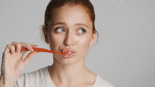 Portrait of beautiful redhead girl intently brushing teeth on camera over white background