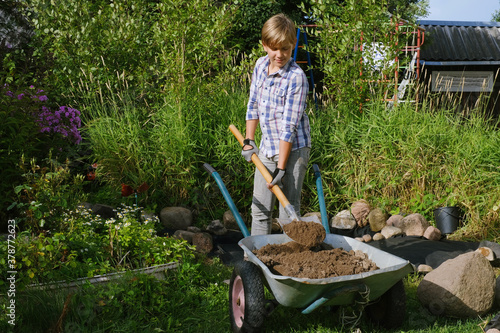Boy working with the shovel and overloading the ground into the wheelbarrow