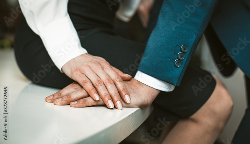 Passionate affair in the office workplace concept. Girl in a skirt sits at the edge of the table. Man stands close to her. High quality photo.