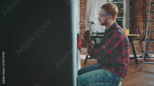 Irritated young man lying on bed cannot rest because of noisy neighbor hammering nail in wall photo