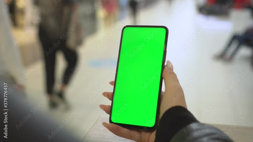 Shopping center. Back view of brunette holding chroma key green screen smartphone watching content. Gadgets and contemporary people concept. Shopping center. Back view of brunette holding chroma key green screen smartphone watching content. Gadgets and contemporary people concept.