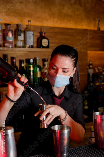 young woman bartender makes cocktail with medical mask and protection against coronavirus COVID-19.
