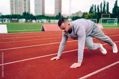 Strong caucasian male in grey tracksuit pushing from surface of stadium reaching good results for slimming, serious hipster guy having morning workout making exercises for physical body health