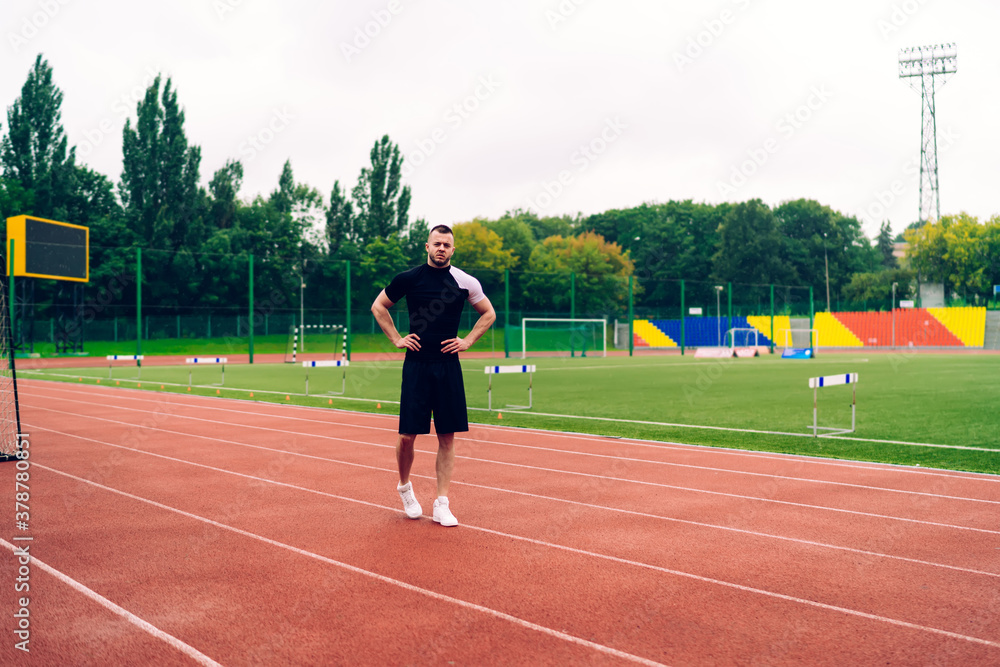 Half length portrait of handsome caucasian male athlete in trendy activewear standing on stadium, strong young sportsman having break on workout resting and having free time keeping healthy lifestyle