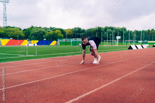 Young caucasian male runner starting spring from point on stadion reaching sport goals on workout, handsome hipster guy athlete concentrated on speed short distance running having morning training