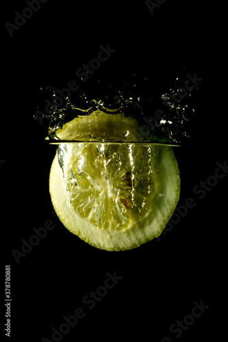 Fresh sliced lemon fruit splashing into clear water isolated black background 