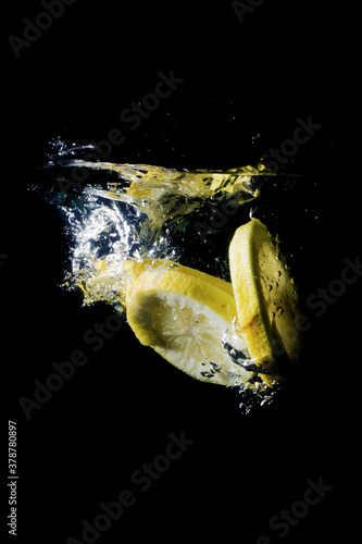 Fresh sliced lemon fruit splashing into clear water isolated black background 