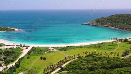 The tropical paradise of the Half moon bay beach on the island of Antigua enclosing a turquoise blue caribbean sea on a sunny summer day, white sand beaches and a palm alley, aerial scenic view 4K. photo