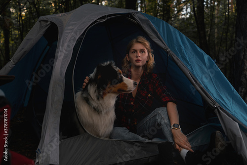 Woman and Aussie Dog Sitting In Tent In Dark Autumnal Forest. Travelling At Native Coutry, Vacation With Closed Borders