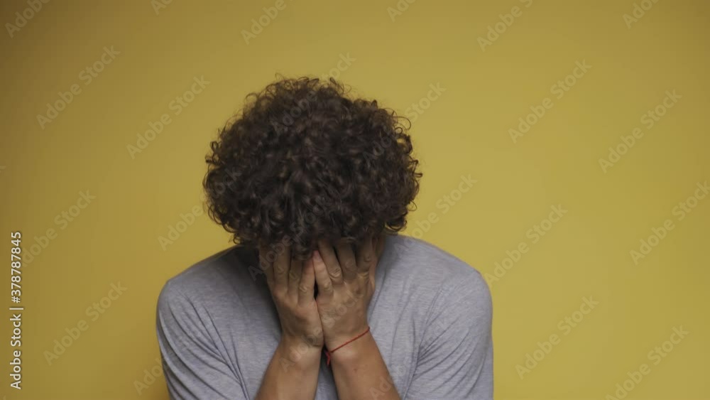 Curly-haired guy sobs with his hands covering his face. Man cries in the studio against an isolated background. Convulsive weeping. High quality 4k footage. Curly-haired guy sobs with his hands covering his face. Man cries in the studio against an isolated background. Convulsive weeping. High quality 4k footage.