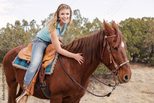 Southwestern theme with a Cowgirl with cowboy hat and chaps Riding brown Horse in the hills and ranch Outdoors in New Mexico