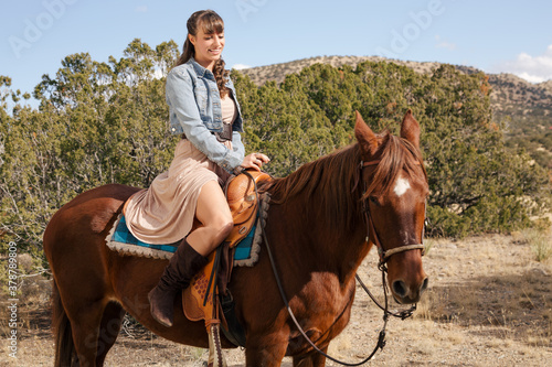 Southwestern theme with a Cowgirl with cowboy hat and chaps Riding brown Horse in the hills and ranch Outdoors in New Mexico © EAPHOTOART