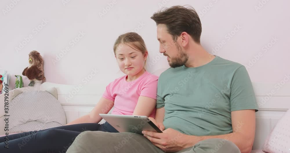 Father and teen daughter sitting on the sofa in living room, browsing the online store, enjoying weekend. Father asks what she thinks about some of articles. Father and teen daughter sitting on the sofa in living room, browsing the online store, enjoying weekend. Father asks what she thinks about some of articles.