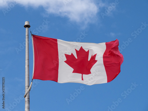 a Canada flag waving gently on a blue sky with a single cloud