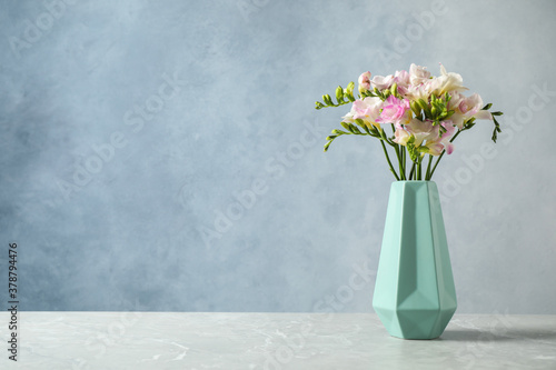 Beautiful blooming freesias in vase on table against blue background. Space for text