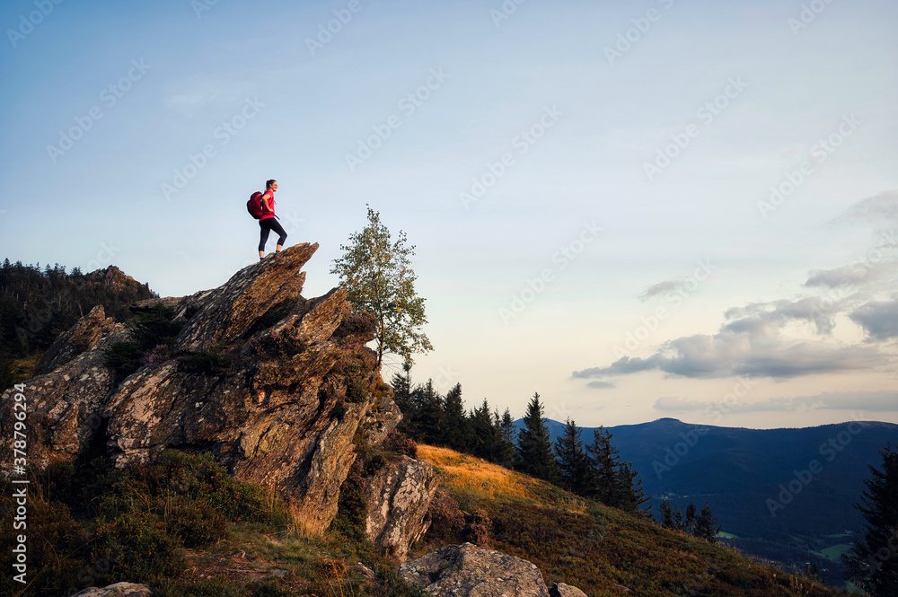 Junge, sportliche Frau steht am Gipfel und genießt den Sonnenuntergang am Osser