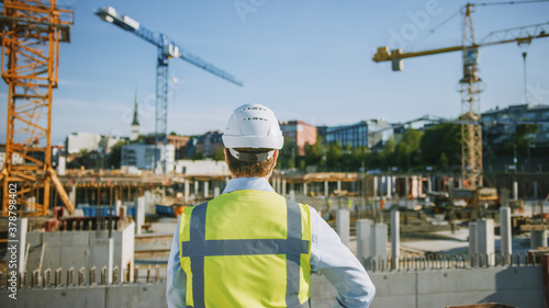 Foto Confident Bearded Head Civil Engineer-Architect in Sunglasses is Standing Outside with His Back to Camera in a Construction Site on a Bright Day
