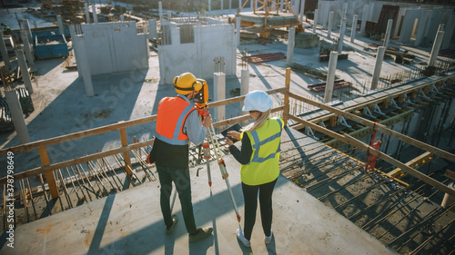 Foto Construction Worker Using Theodolite Surveying Optical Instrument for Measuring Angles in Horizontal and Vertical Planes on Construction Site