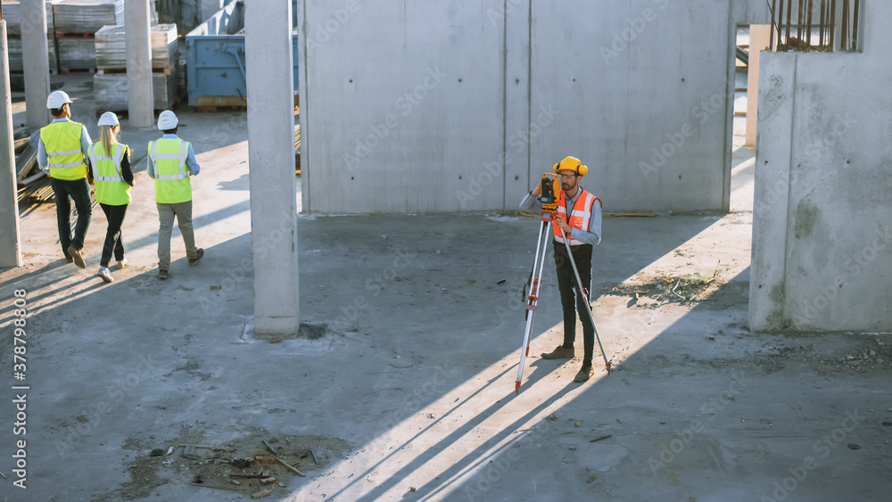Construction Worker Using Theodolite Surveying Optical Instrument for Measuring Angles in Horizontal and Vertical Planes on Construction Site. Worker in Hard Hat Making Projections for the Building. Construction Worker Using Theodolite Surveying Optical Instrument for Measuring Angles in Horizontal and Vertical Planes on Construction Site. Worker in Hard Hat Making Projections for the Building.