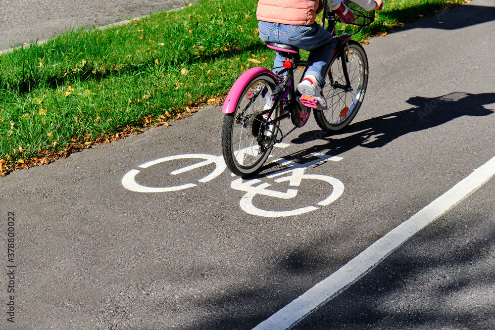 The girl rides the pink bicycle on the bike path in autumn in sunny weather.