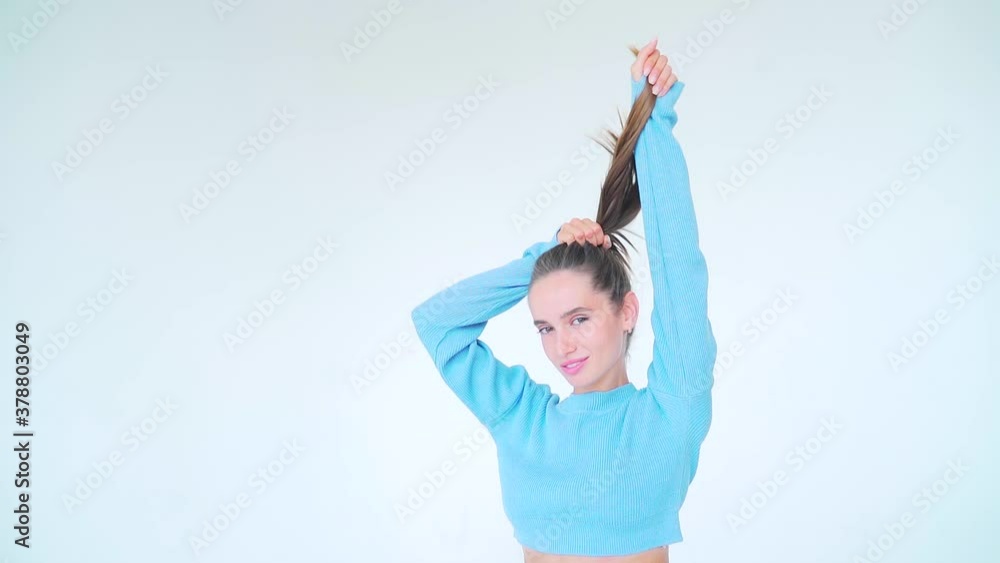 Portrait of a young attractive fashion model woman with natural long hair in blue clothes on a white background. posing and looking at the camera. shakes hands holding hair up. Makeup natural beauty Portrait of a young attractive fashion model woman with natural long hair in blue clothes on a white background. posing and looking at the camera. shakes hands holding hair up. Makeup natural beauty