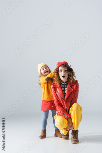 mother and daughter in colorful red and yellow outfits having fun on grey background