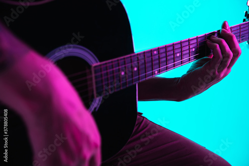 Close up of guitarist hand playing guitar, macro. Concept of advertising, hobby, music, festival, entertainment. Person improvising inspired. Copyspace to insert image or text. Colorful neon lighted.