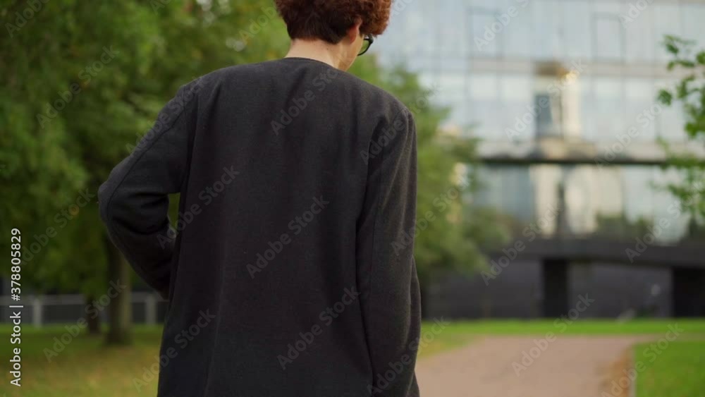 Tilt up panning shot of stylish young man with briefcase in his hand walking down footpath in slow motion, text messaging on cell phone and smiling Tilt up panning shot of stylish young man with briefcase in his hand walking down footpath in slow motion, text messaging on cell phone and smiling
