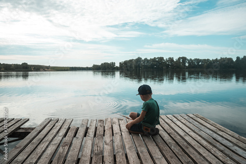 Boy sitting alone on pier while fishing from dock on lake. Kid on beautiful morning in nature © shara