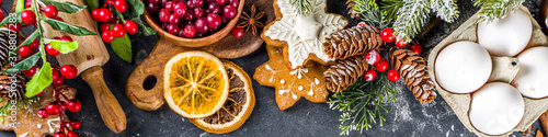 Fototapeta Naklejka Na Ścianę i Meble -  Ingredients for Christmas cooking, winter baking cookies, gingerbread, fruitcake, seasonal drinks. Cranberries, dried oranges, cinnamon, spices, flour on dark stone table, copy space top view