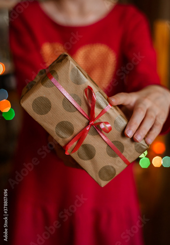 Christmas background with gift boxes, balls of rope, paper rolls and decorations on red. Preparing gifts for Christmas. Children's hands holding a gift box, top view.