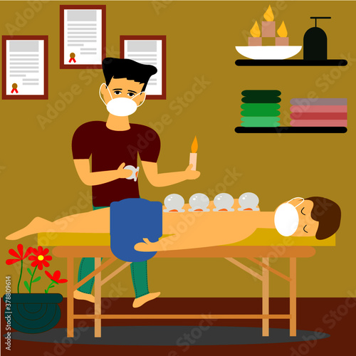 Relaxed Young man  receiving cupping therapy from practitioner  with wearing medical face mask due to ongoing pandemic of coronavirus, covid-19.

