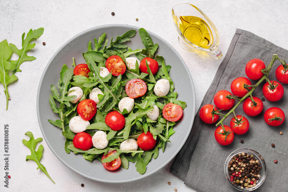 Diet and healthy salad with arugula, cherry tomatoes, mozzarella cheese and olive oil on white background Diet and healthy salad with arugula, cherry tomatoes, mozzarella cheese and olive oil on white background