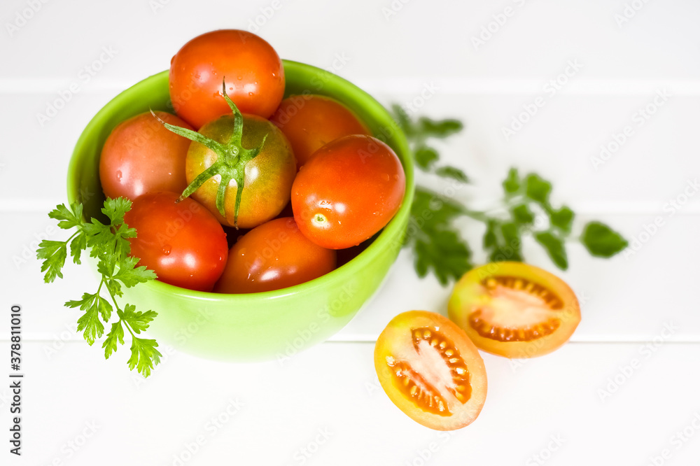 ripe tomatoes in a bowl on a white background and sprigs of parsley. tomatoes on a white background close-up. tomato halves and whole tomatoes on the table. ripe tomatoes in a bowl on a white background and sprigs of parsley. tomatoes on a white background close-up. tomato halves and whole tomatoes on the table.