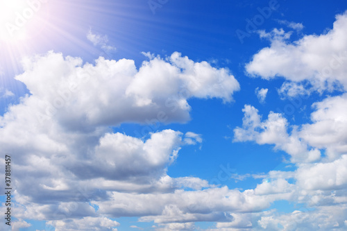 white fluffy cumulus clouds on blue sky with sun rays