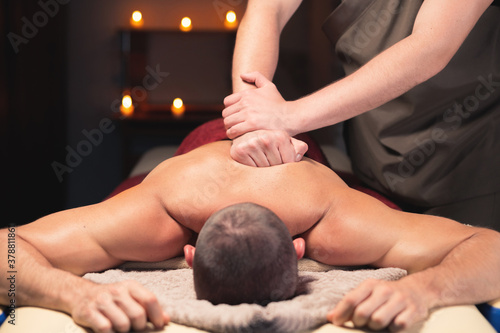 Back massage. Male masseur doing back massage to male client in dark room of spa salon