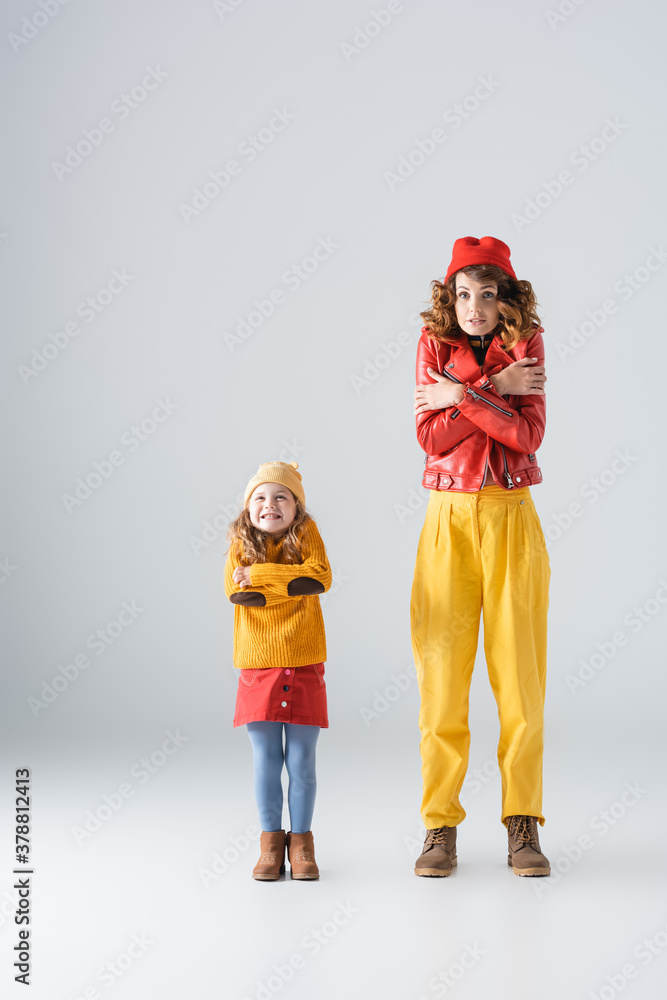 mother and daughter in colorful red and yellow outfits feeling cold on grey background