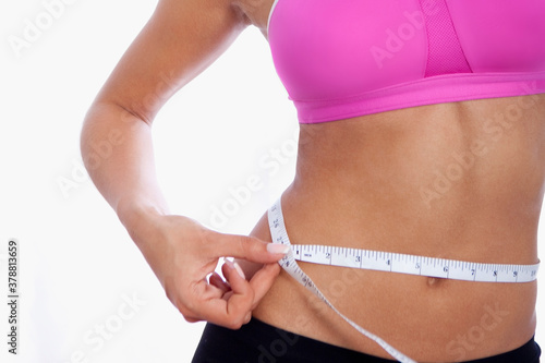 Mid section view of a woman measuring her waistline with a measuring tape