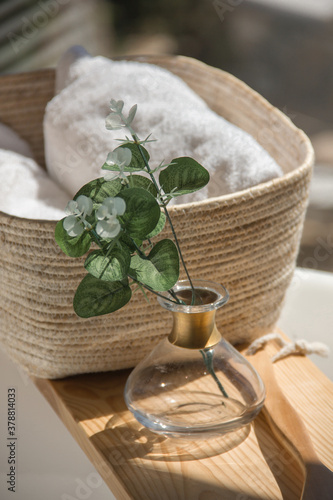 close-up white bath towels in a wicker basket next to accessories on a wooden shelf in the white bathroom at morning