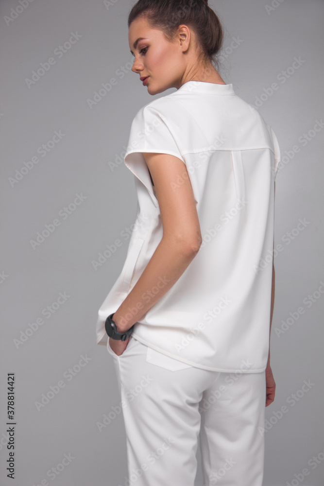 young stylish brunette nurse in white medical costume is standing from the back and looking away on the gray background. medical fashion concept, free space on left side young stylish brunette nurse in white medical costume is standing from the back and looking away on the gray background. medical fashion concept, free space on left side