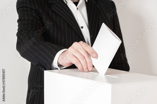 The hand drops the Bulletin into the slot of the box. A person takes part in elections. The voter puts the ballot in the ballot box on a light background. The concept of freedom and democracy.