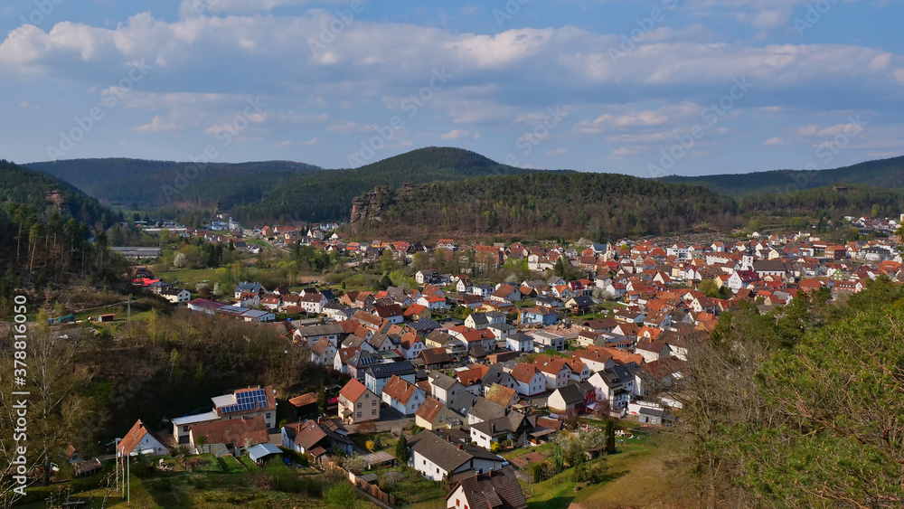 Panorama view over village Dahn (Palatinate Forest, Rhineland-Palatinate, Germany), located in a valley surrounded by forests and hills with big sandstone formation in background at sunny spring day.